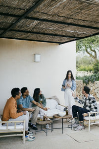 Multiracial friends talking while sitting at patio in backyard during party