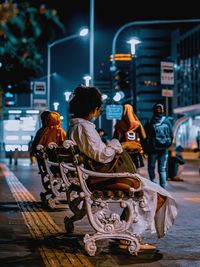 Rear view of man sitting on illuminated street at night