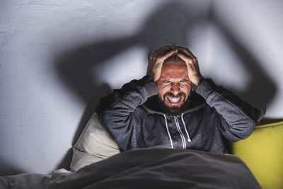 Angry man with headache sitting on bed