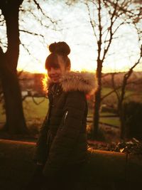 Portrait of girl standing against bare trees during sunset