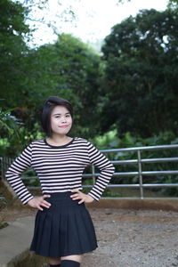 Portrait of smiling young woman standing on field against trees in forest