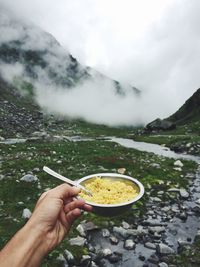Close-up of cropped hand holding noodles in bowl against mountains at manali
