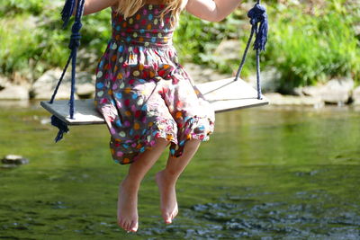 Low section of girl swinging over lake