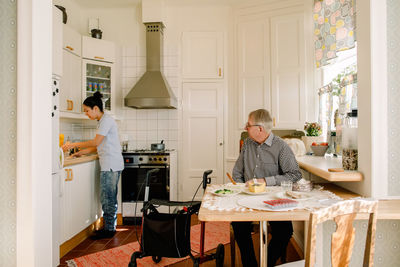 Retired senior man looking at young female caregiver working in kitchen