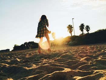 Rear view of woman walking on sand against sky