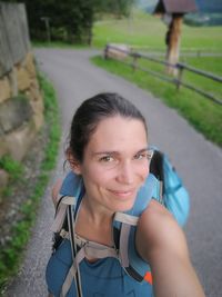 High angle portrait of smiling hiker standing on road by field