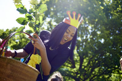 Happy woman wearing paper crown while carrying basket during birthday celebration at backyard