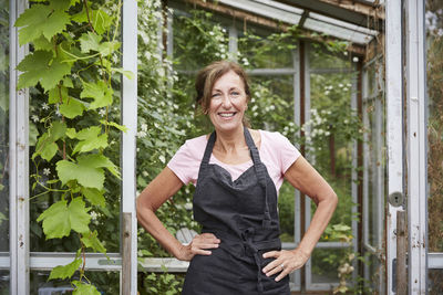 Portrait of happy senior gardener standing with hands on hips at yard