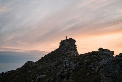 Low angle view of rocks on cliff against sky during sunset