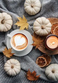 White pumpkins, coffee and autumn leaves on a grey knitted sweater. autumn home decor.