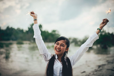 Portrait of smiling young woman standing in water against sky