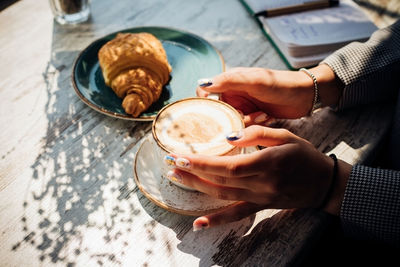 Cappuccino and croissant on the table in the cafe.women's hands hold a cup of coffee.