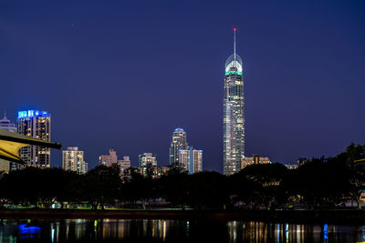 Illuminated buildings by river against sky at night