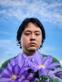 Portrait of young man behind purple clematis flowers against blue sky.