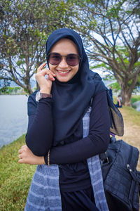 Portrait of young woman wearing sunglasses standing against trees