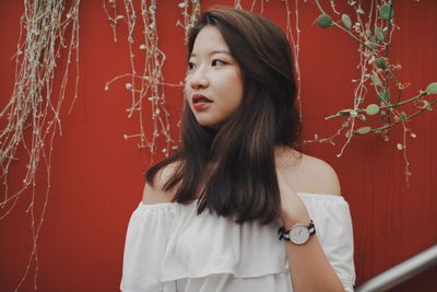 Close-up of young woman standing against red wall