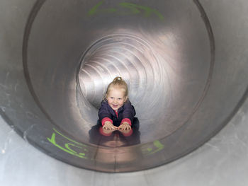 Smiling girl sliding in tube while looking away at playground