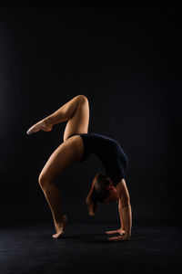 Side view of woman exercising against black background