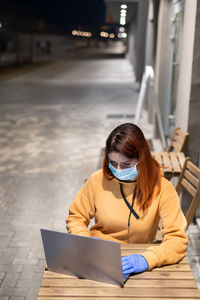 High angle view of businesswoman wearing mask using laptop in cafe at night