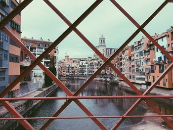 River amidst buildings against sky seen through fence