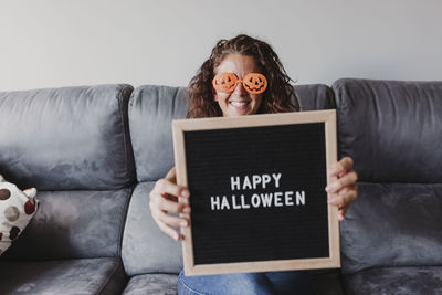 Portrait of woman in novelty glasses holding happy halloween text at home