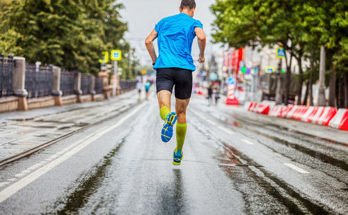 Back man athlete running marathon down street in rainy weather