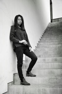 Low angle view of woman standing with camera on steps against wall