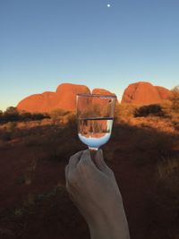 Hand holding glass of mountain against clear sky