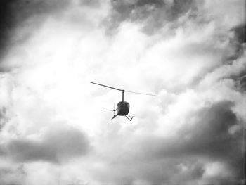 Low angle view of helicopter flying against cloudy sky