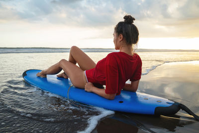 Woman sitting on surfboard on the beach after her surfing session