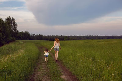 Mom and daughter in white t-shirts and denim shorts have fun on a green field in summer