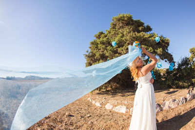 Woman with arms outstretched standing on land against sky