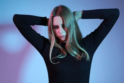 Portrait of young woman with arms raised against sky