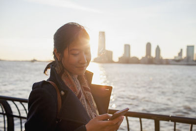 Young asian businesswoman looking at her smartphone standing on river promenade