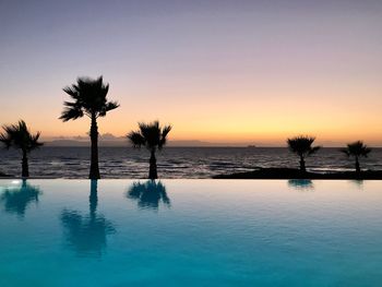 Silhouette palm tree by swimming pool against sky during sunset