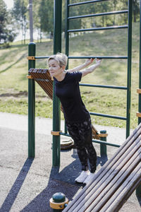 Woman stretching hands while practicing exercise at park during sunny day