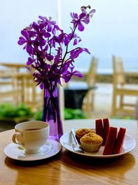 Coffee cup and purple roses in vase on table