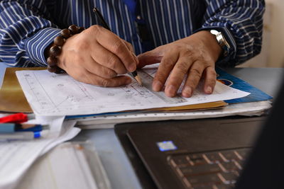 Midsection of architect drawing blueprint at desk