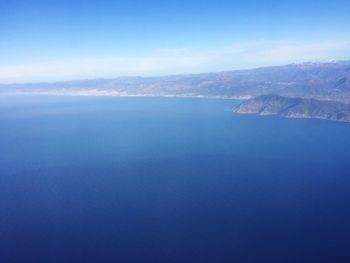 Aerial view of sea and mountains against blue sky