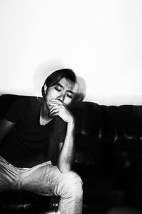 Young man smoking while sitting against wall