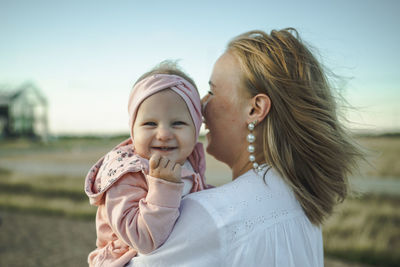 Happy cute baby girl with mother standing in front of sky