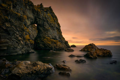 Rock formation in sea against sky during sunset