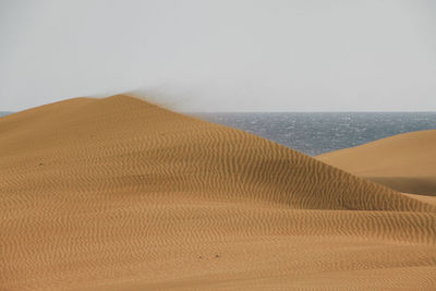 Sand dunes by sea against sky at grand canary