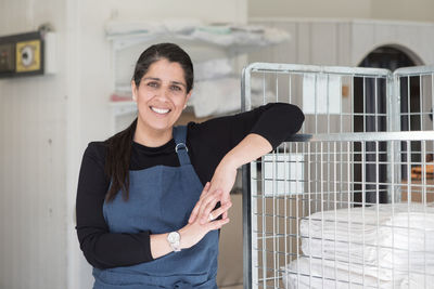 Portrait of smiling confident mature female entrepreneur standing by rack at laundromat