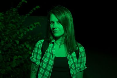 Portrait of young woman standing against black background