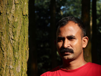 Close-up portrait of man against tree trunk