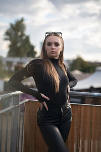 Portrait of young woman standing against railing