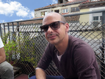 Portrait of man wearing sunglasses against fence