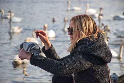 Pigeon perching on woman hand at lakeshore