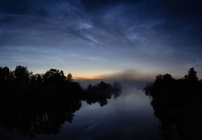 Silhouette trees by lake against sky during sunset